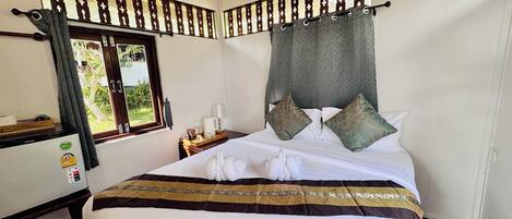 A hotel room with a bed, a desk, a refrigerator, and a window with curtains.