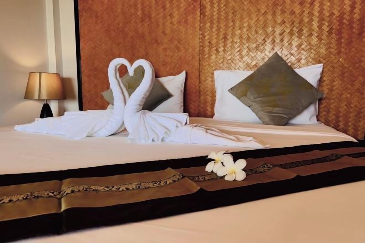 A neatly made bed with white linens and a heart-shaped towel arrangement.
