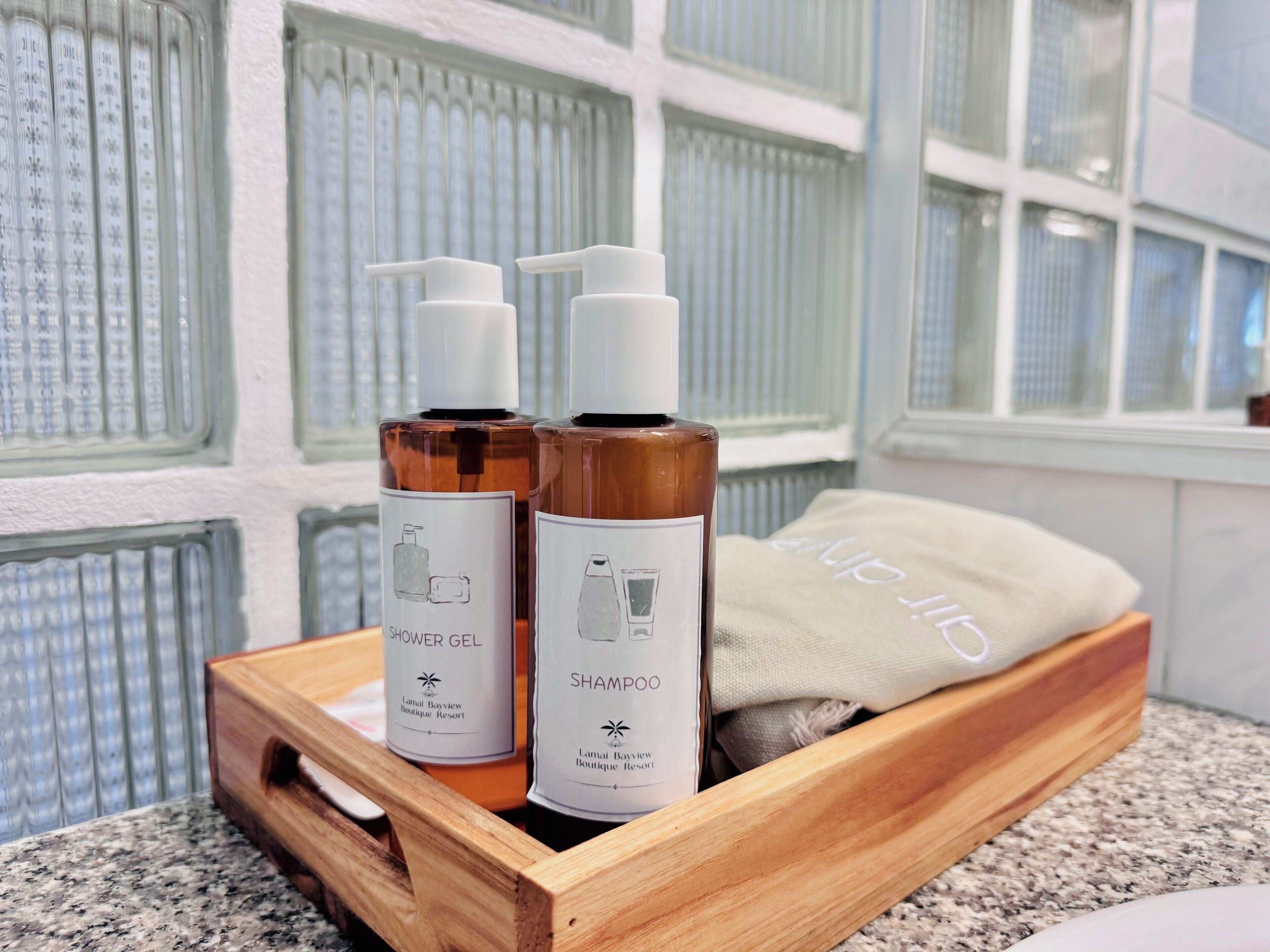 A wooden tray with two bottles of shower gel and shampoo, and a towel on a granite countertop.