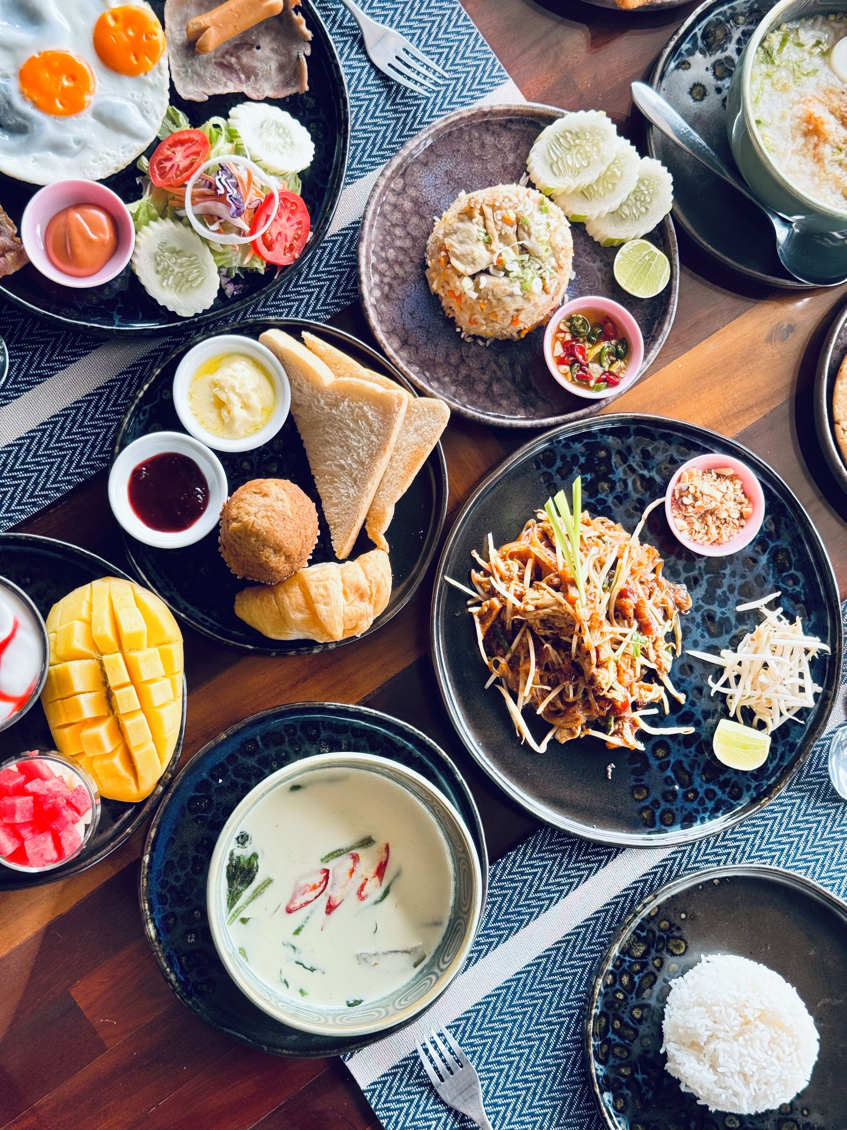 A variety of dishes including fried eggs, rice, and a bowl of soup, arranged on a table with a patterned tablecloth.