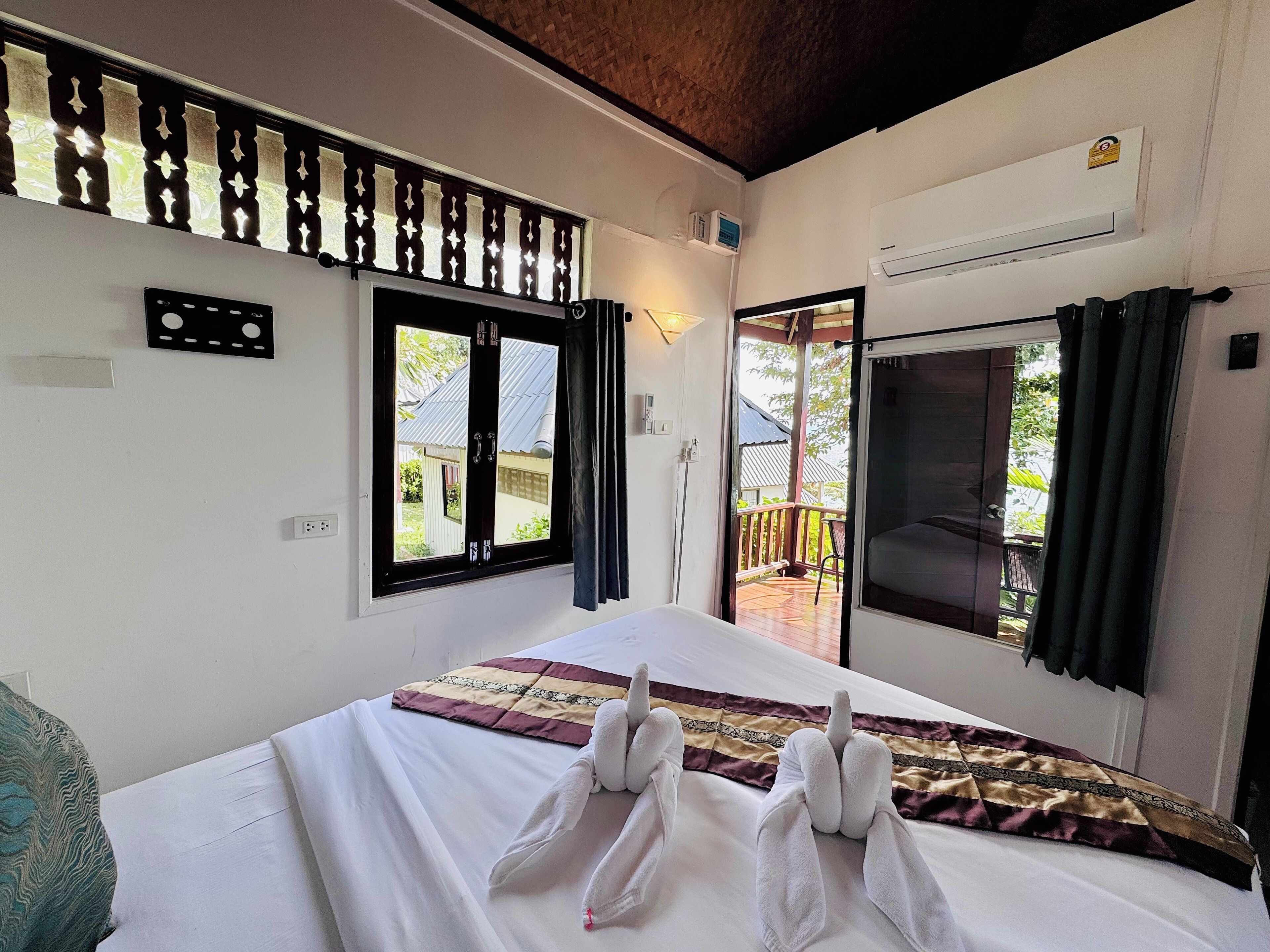 A hotel room with a bed, a window with a view of the outside, an air conditioning unit, and a balcony with a railing.