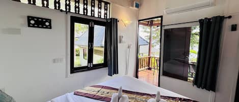 A hotel room with a bed, a window with a view of the outside, an air conditioning unit, and a balcony with a railing.