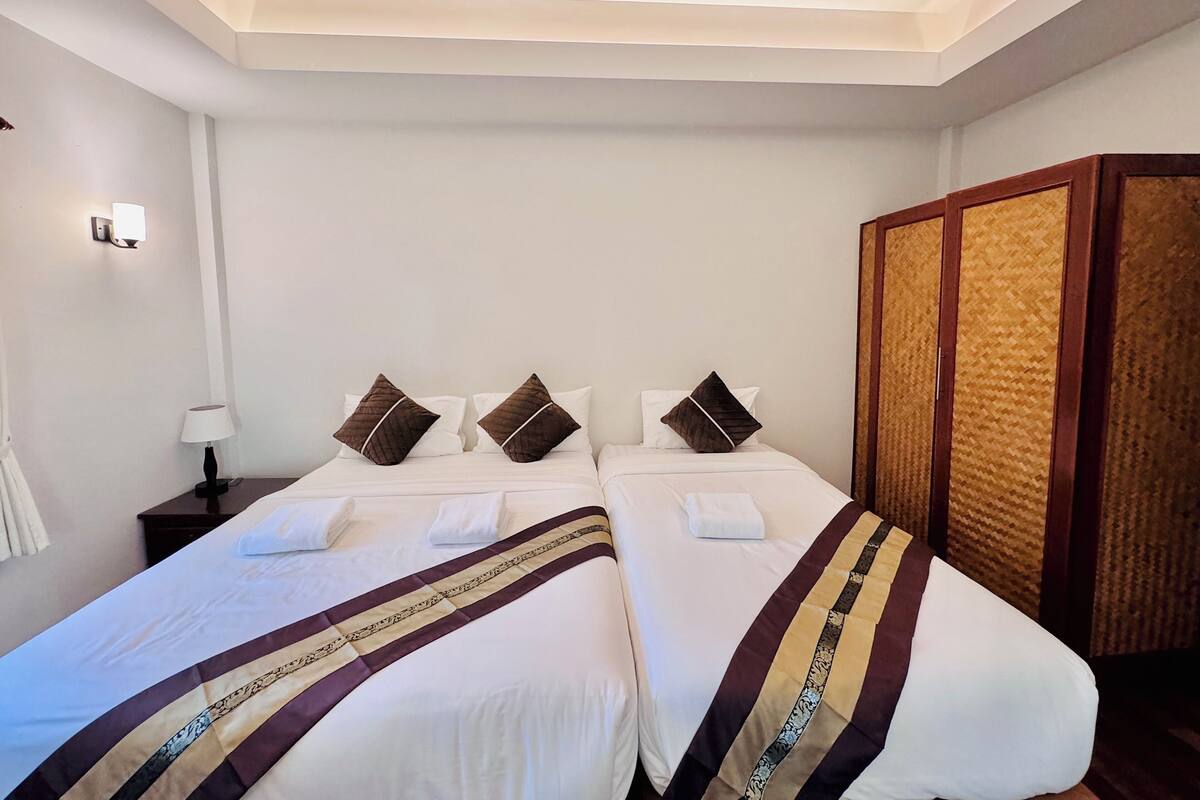 Quarto de hotel com duas camas, uma mesa de cabeceira, uma luminária e um guarda-roupa.