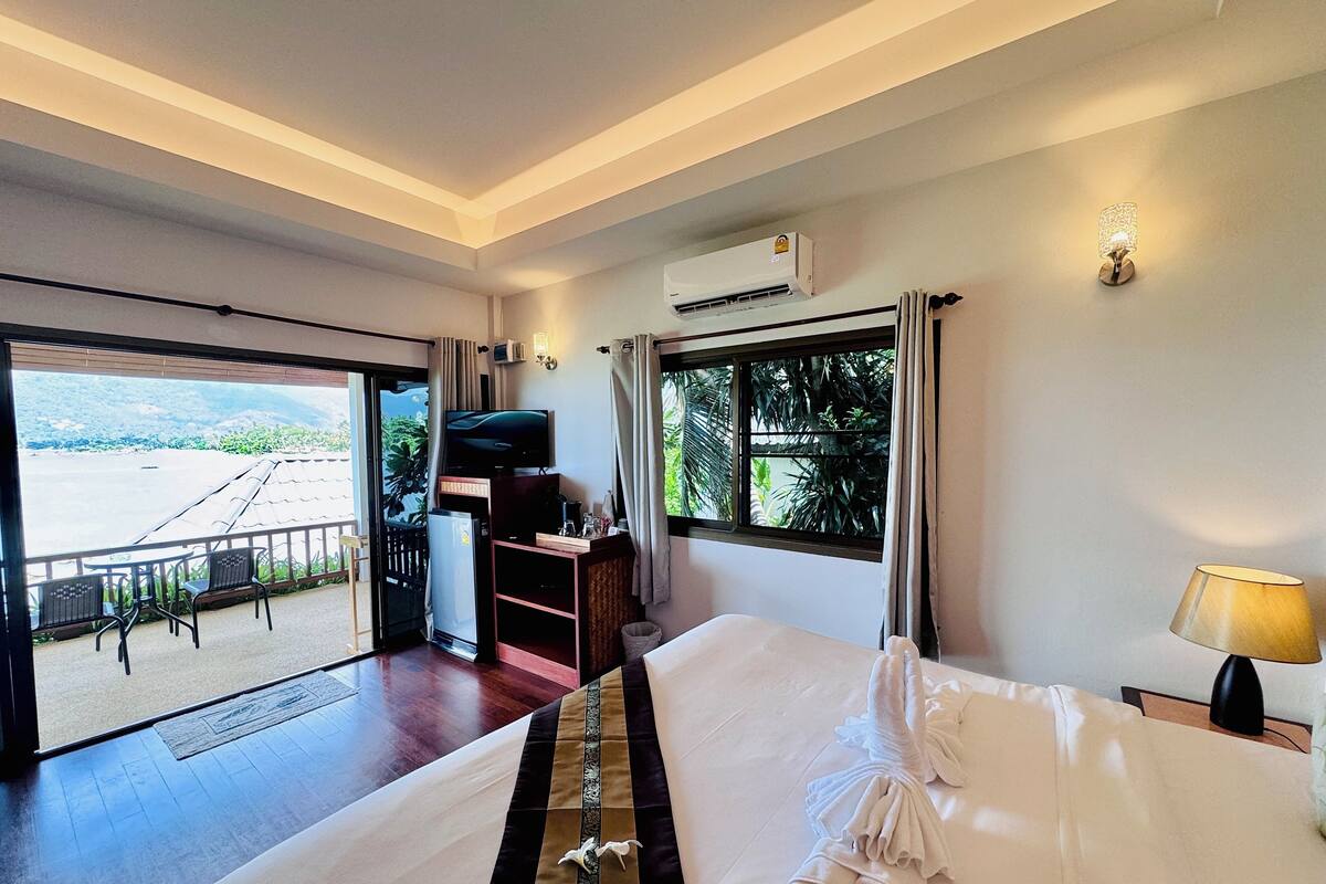 Quarto de hotel com uma cama grande, televisão, frigorífico e varanda com vista para o mar.