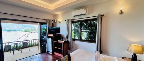 Habitación de hotel con una cama grande, televisión, refrigerador y balcón con vistas al mar.