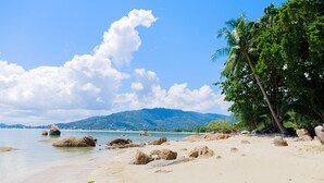 Una playa con rocas grandes, agua azul cristalina y palmeras.