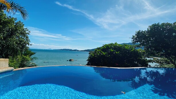 Una piscina infinita azul cristalina con vistas al mar y montañas al fondo.