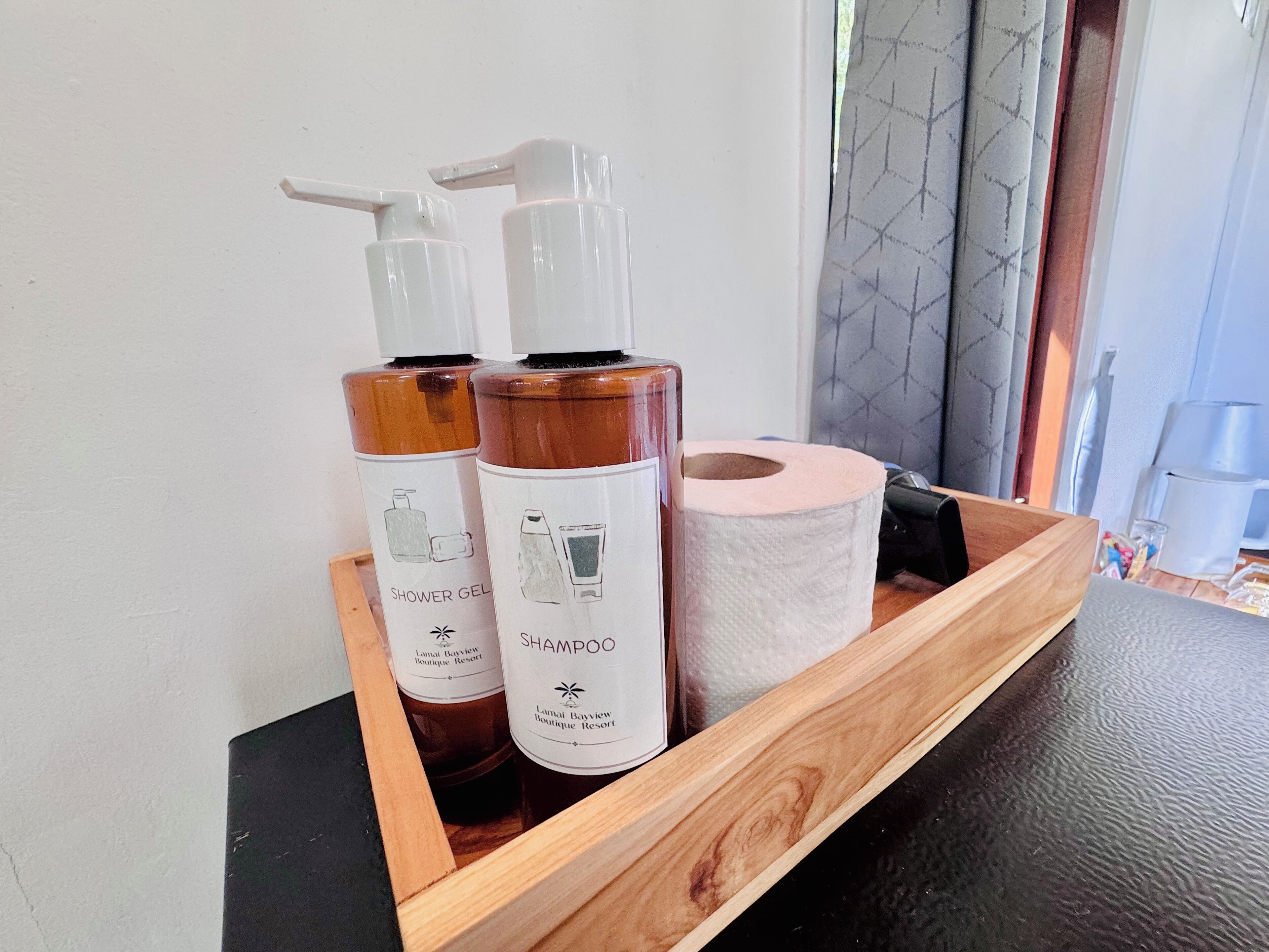 A wooden tray with two bottles of shampoo and a roll of toilet paper.