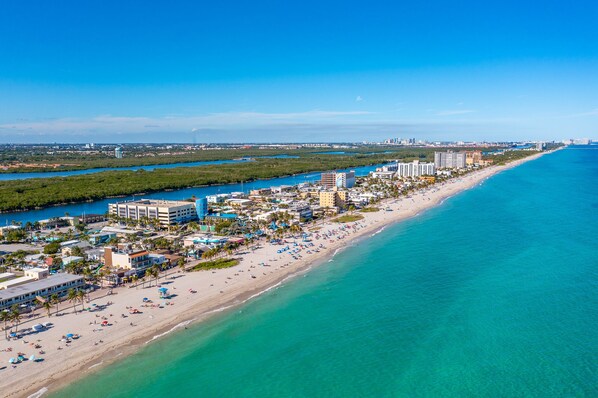 Vista aérea de una ciudad costera con una playa extensa, aguas azules cristalinas y una zona urbana densa con edificios altos y hoteles.