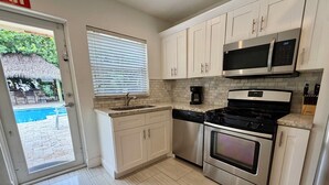 A modern kitchen with stainless steel appliances, white cabinetry, and a view of a pool outside. - 3/3 Duplex for 6+Shared Heated Pool, Tiki Bar BBQ (Hollywood)