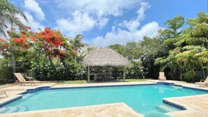 A swimming pool with a thatched-roof gazebo, lounge chairs, and tropical vegetation. - 3/3 Duplex for 6+Shared Heated Pool, Tiki Bar BBQ (Hollywood)