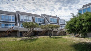 A row of modern multi-story residential buildings with external staircases, a grassy courtyard, and a large tree. - Close to the beach with community pool! (Lewes)