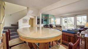 A spacious living area with a round glass-top table, wooden chairs, a staircase, and a view of the outside. - Close to the beach with community pool! (Lewes)