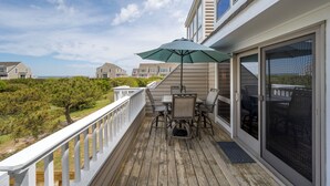 A wooden deck with a table and chairs, a green umbrella, and a view of houses and trees. - Close to the beach with community pool! (Lewes)
