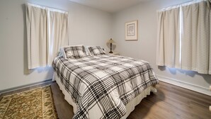 Un dormitorio con cama, cortinas, alfombra, mesita de noche y lámpara de pared.