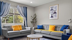 A modern living room with two grey sofas, a round coffee table, and blue and yellow cushions.