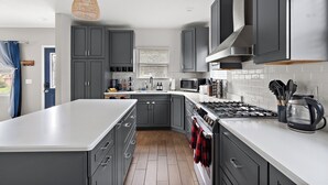 A modern kitchen with grey cabinets, a white countertop, a stove, and a hanging light fixture.