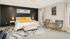 A modern bedroom with a large bed, bedside tables, a bench, and a seating area with chairs.