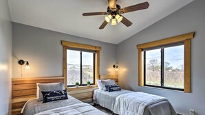 A bedroom with two beds, a ceiling fan, and large windows with a view of the outdoors. - Palisade Cottage on Orchard - Hike, Bike + More! (Palisade)