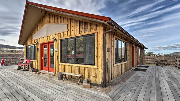 A wooden cabin with a red door, large windows, and a deck. - Palisade Cottage on Orchard - Hike, Bike + More! (Palisade)