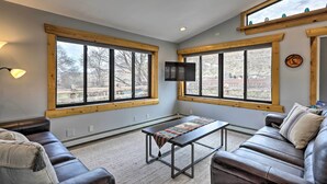 A cozy living room with a large window, a sofa, a coffee table, and a TV mounted on the wall. - Palisade Cottage on Orchard - Hike, Bike + More! (Palisade)