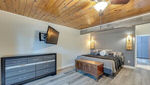 A bedroom with a wooden ceiling, a bed with a headboard, a dresser, and two wall-mounted lights.