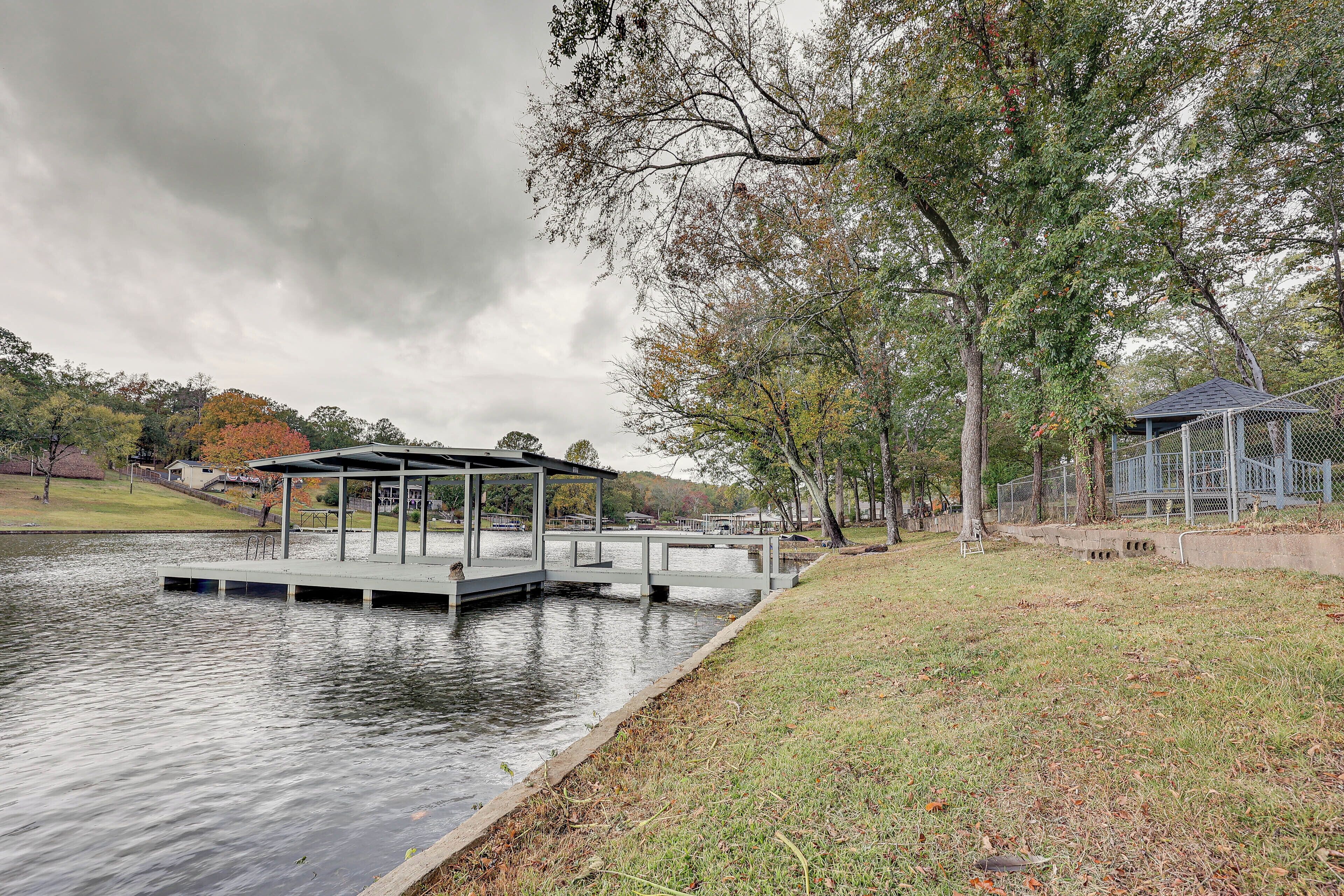 Un parque junto al lago con un pabellón, un muelle y un área cercada con un pequeño edificio.