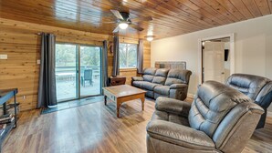 A spacious living room with wooden floors, leather recliners, a wooden coffee table, and a ceiling fan.