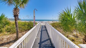 A wooden boardwalk leading to a beach with palm trees and a clear blue sky. - Oceanfront Murrells Inlet Home w/ Beach Access! (Murrells Inlet)