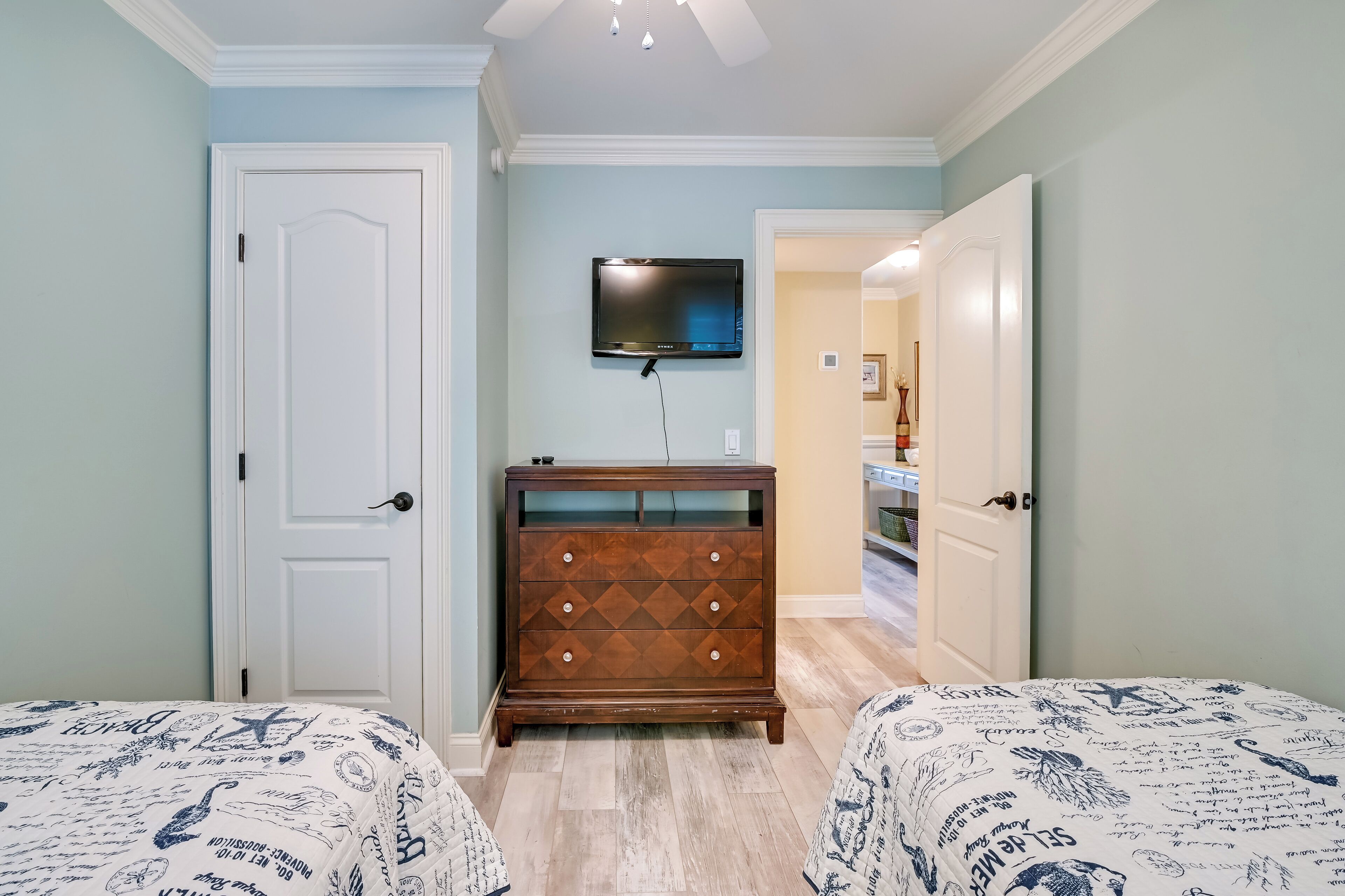 A bedroom with two beds, a dresser, and a TV on the wall.