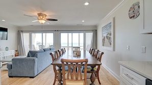 A spacious dining area with a long wooden table and matching chairs, a gray sofa, and a ceiling fan. - Oceanfront Murrells Inlet Home w/ Beach Access! (Murrells Inlet)
