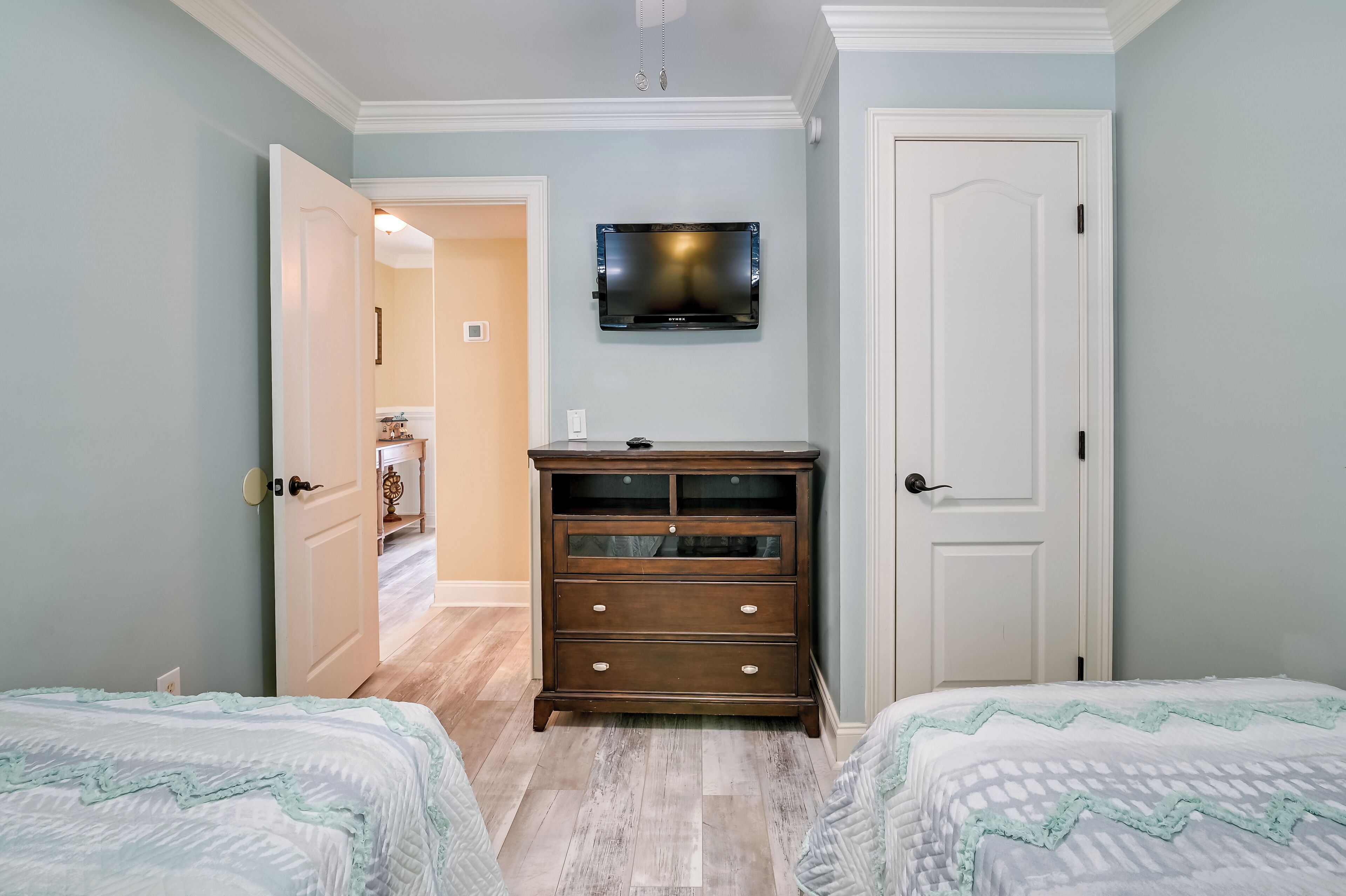 Un dormitorio con dos camas, un aparador, un televisor montado en la pared y una puerta que da a otra habitación.