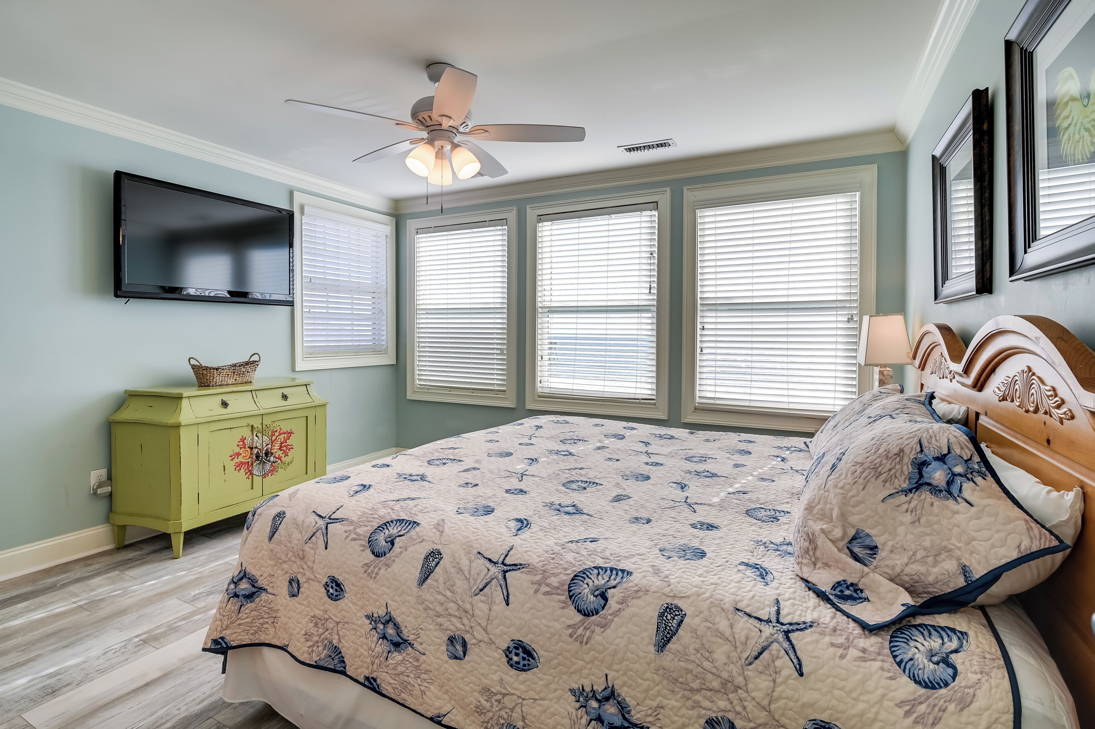Un dormitorio con una cama, ventilador de techo, televisión y cómoda.