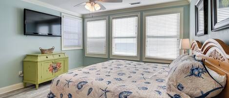 A bedroom with a bed, a ceiling fan, a TV, and a dresser.