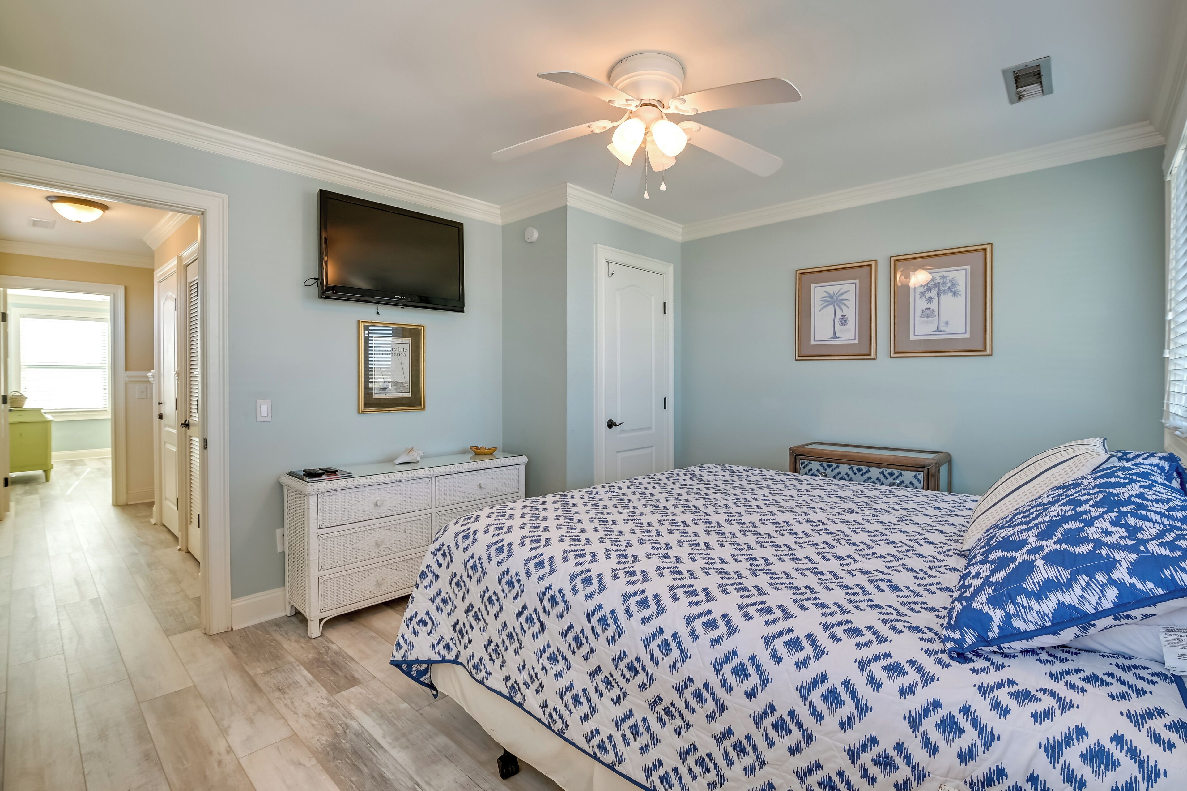 A bedroom with a bed, a ceiling fan, a TV, and framed pictures on the wall.