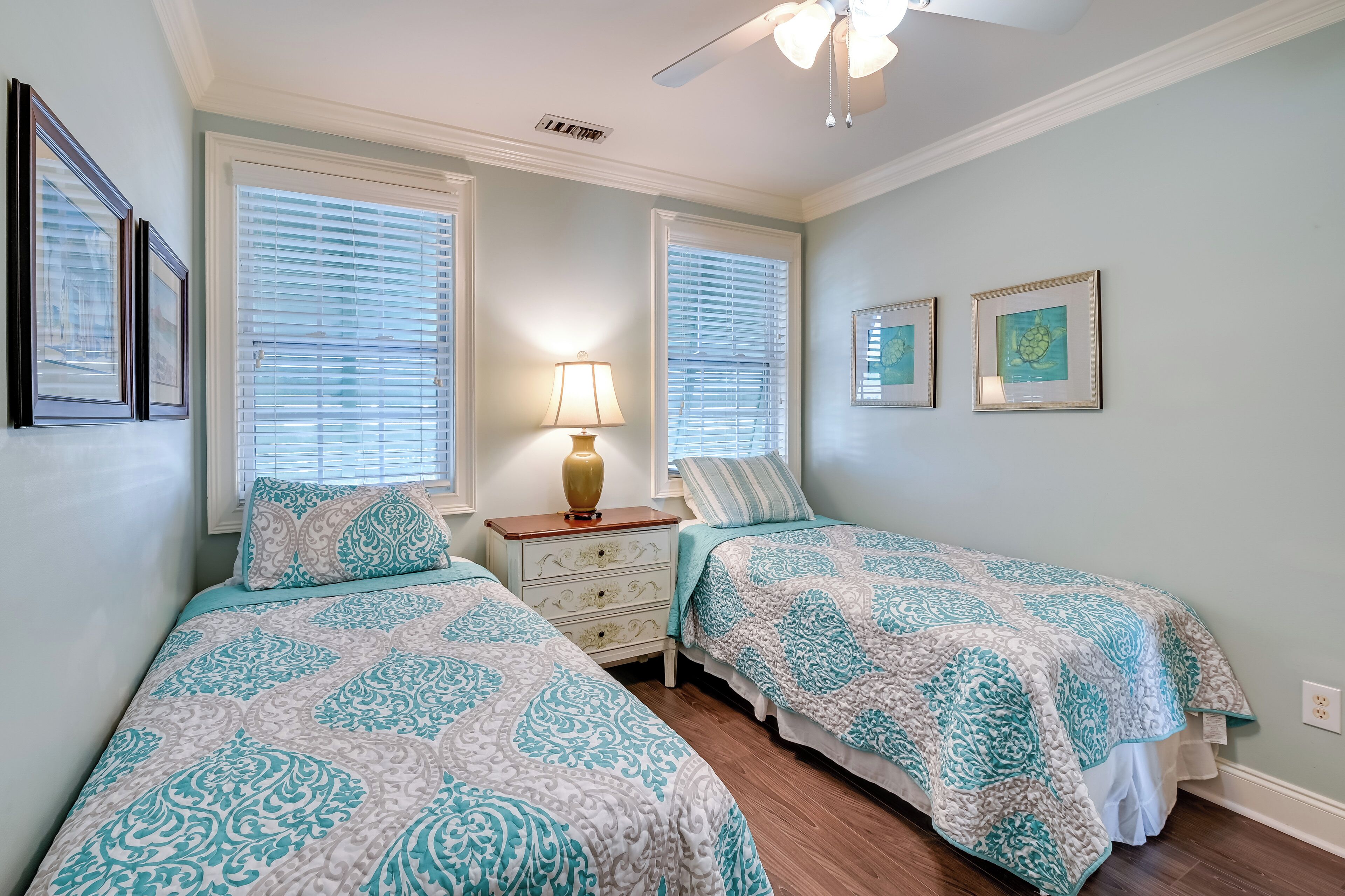 A bedroom with two beds, a nightstand, a lamp, and framed artwork on the wall.