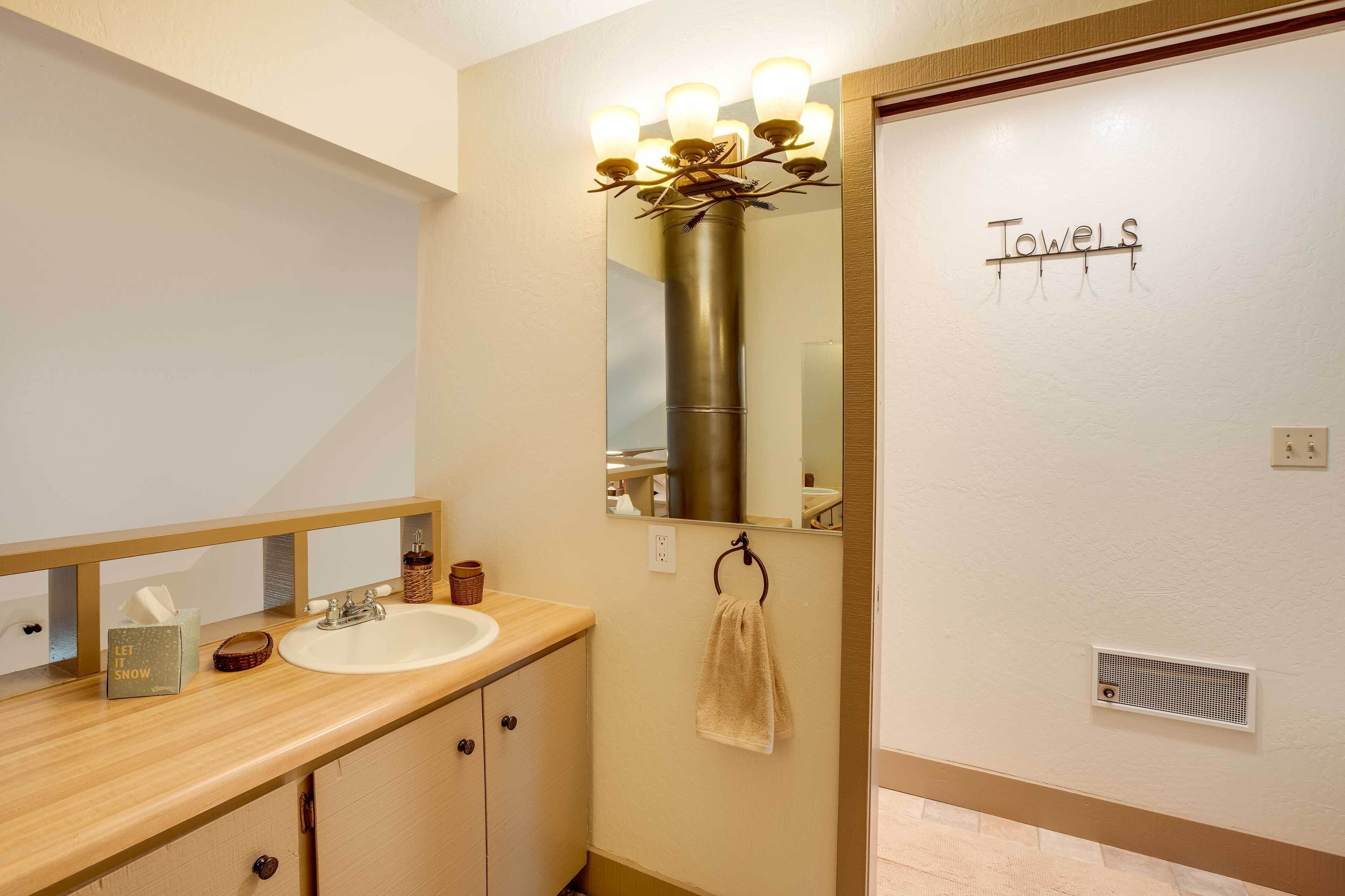 A bathroom with a wooden vanity, a mirror with lights, a towel rack, and a sign that says "Towels".