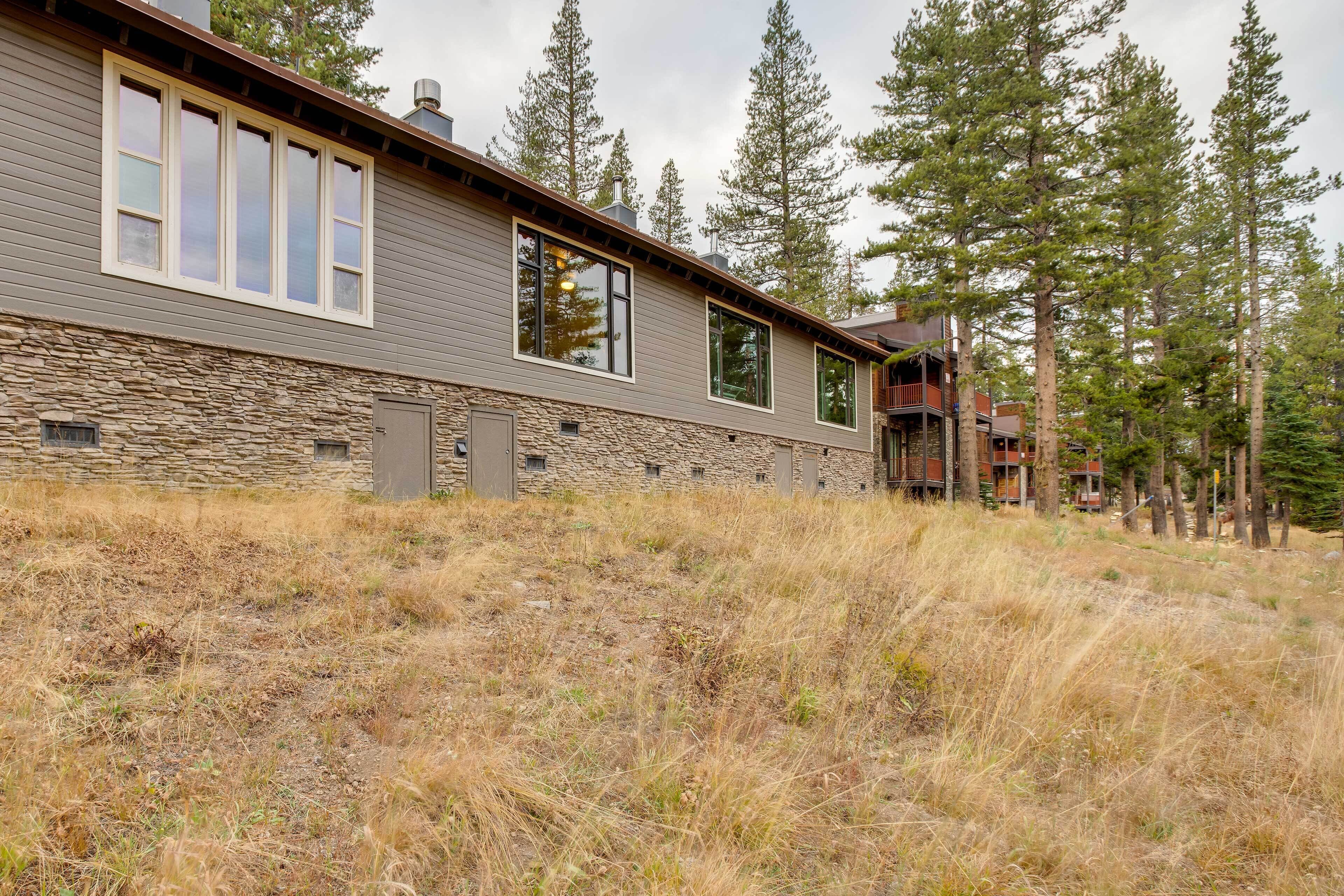 Una casa moderna de dos pisos con base de piedra y ventanas amplias, rodeada de altos pinos.