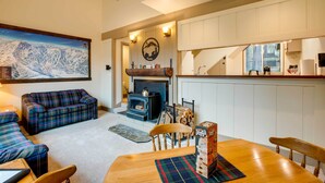 A cozy living room with a fireplace, plaid furniture, and a dining area with a wooden table and chairs. - Mountain Condo w/ Fireplace in Kirkwood Ski Resort (Kirkwood)