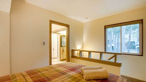 A hotel room with a plaid bedspread, a window with a view of trees, and a door leading to a bathroom. - Mountain Condo w/ Fireplace in Kirkwood Ski Resort (Kirkwood)