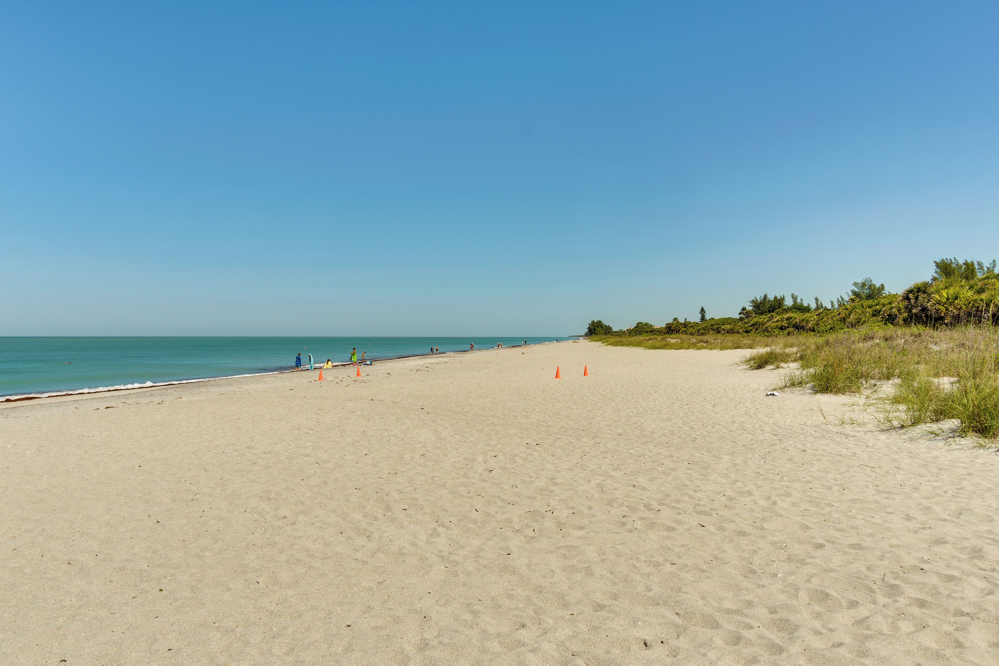 A wide sandy beach with a clear blue sky and calm sea.