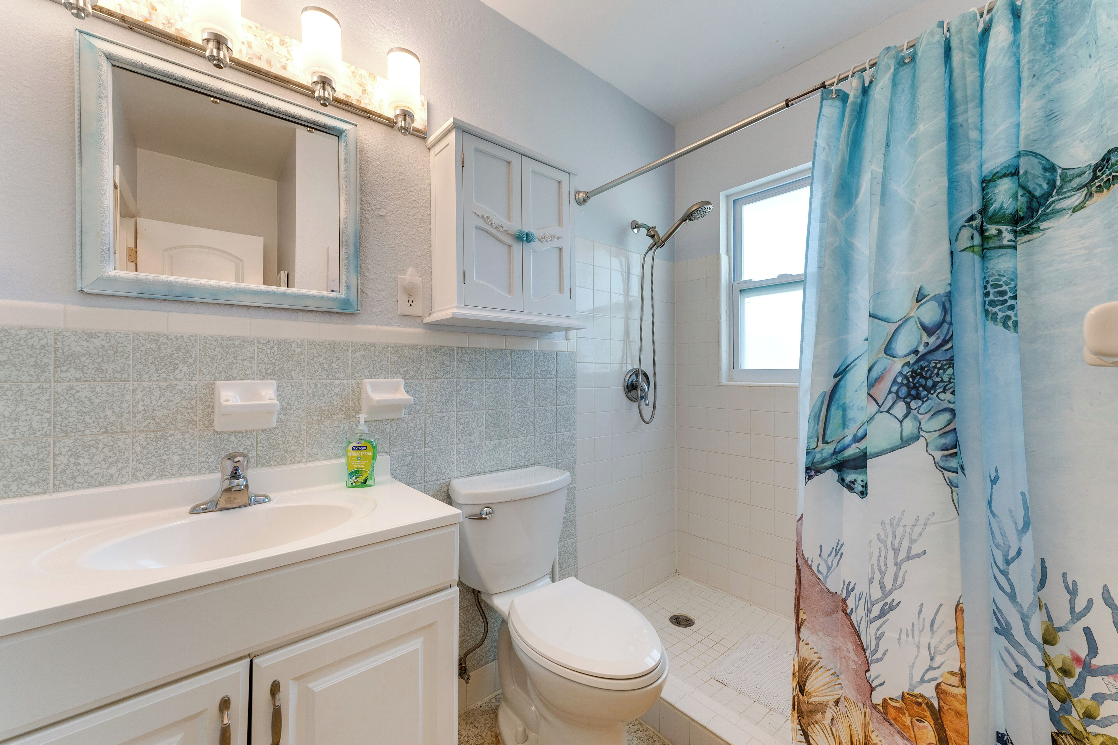 A bathroom with a white sink, a toilet, a shower with a glass door, and a curtain with a sea turtle design.