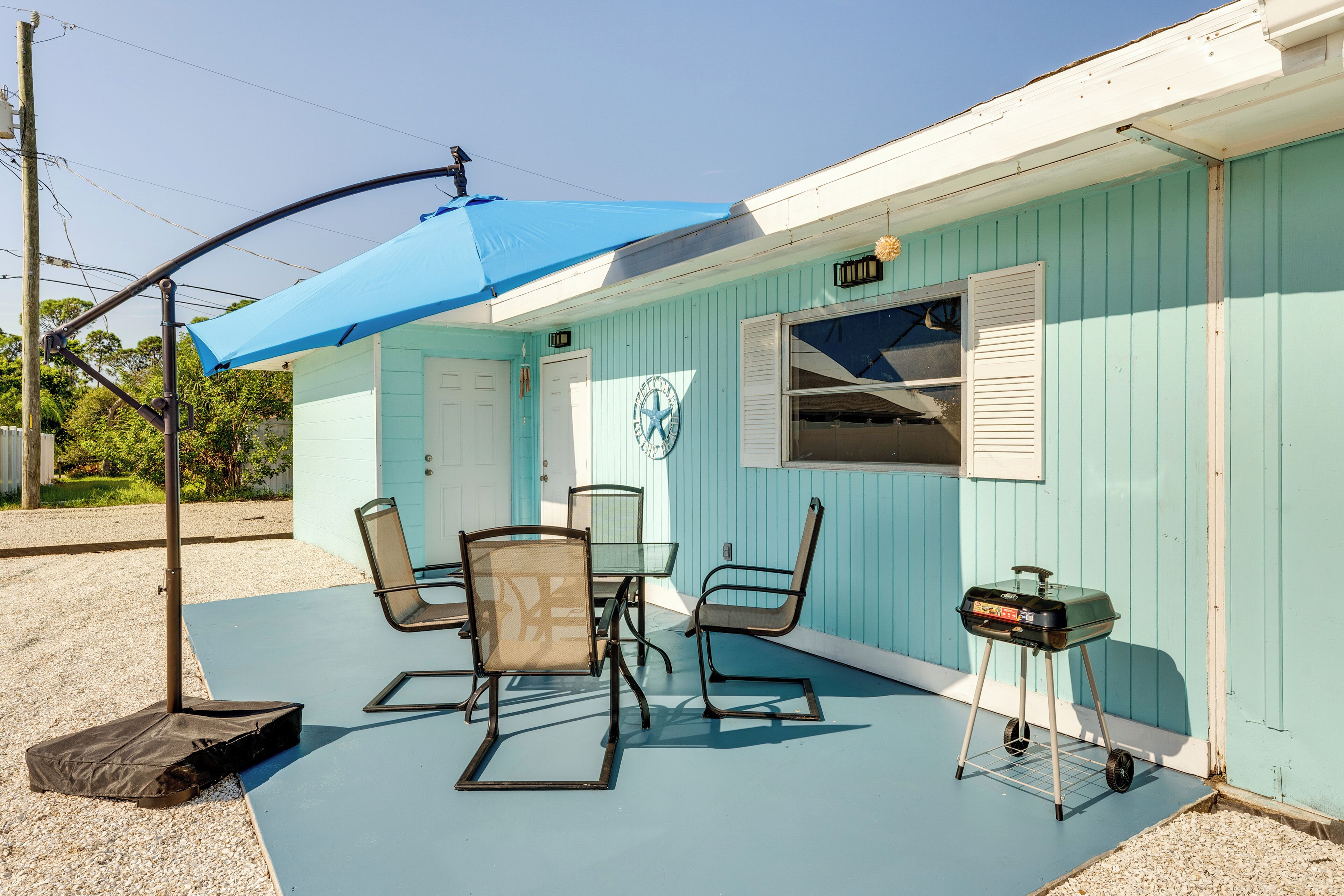 An outdoor patio with a blue umbrella, two chairs, a table, and a grill cart.