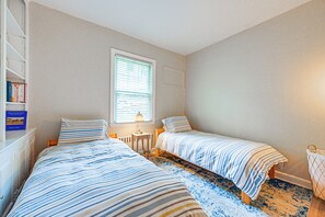 Quarto com duas camas, uma janela, mesa de cabeceira e estante.