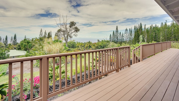 Une terrasse en bois, dotée d’une rambarde, qui offre une vue sur un jardin où poussent différentes plantes et fleurs.