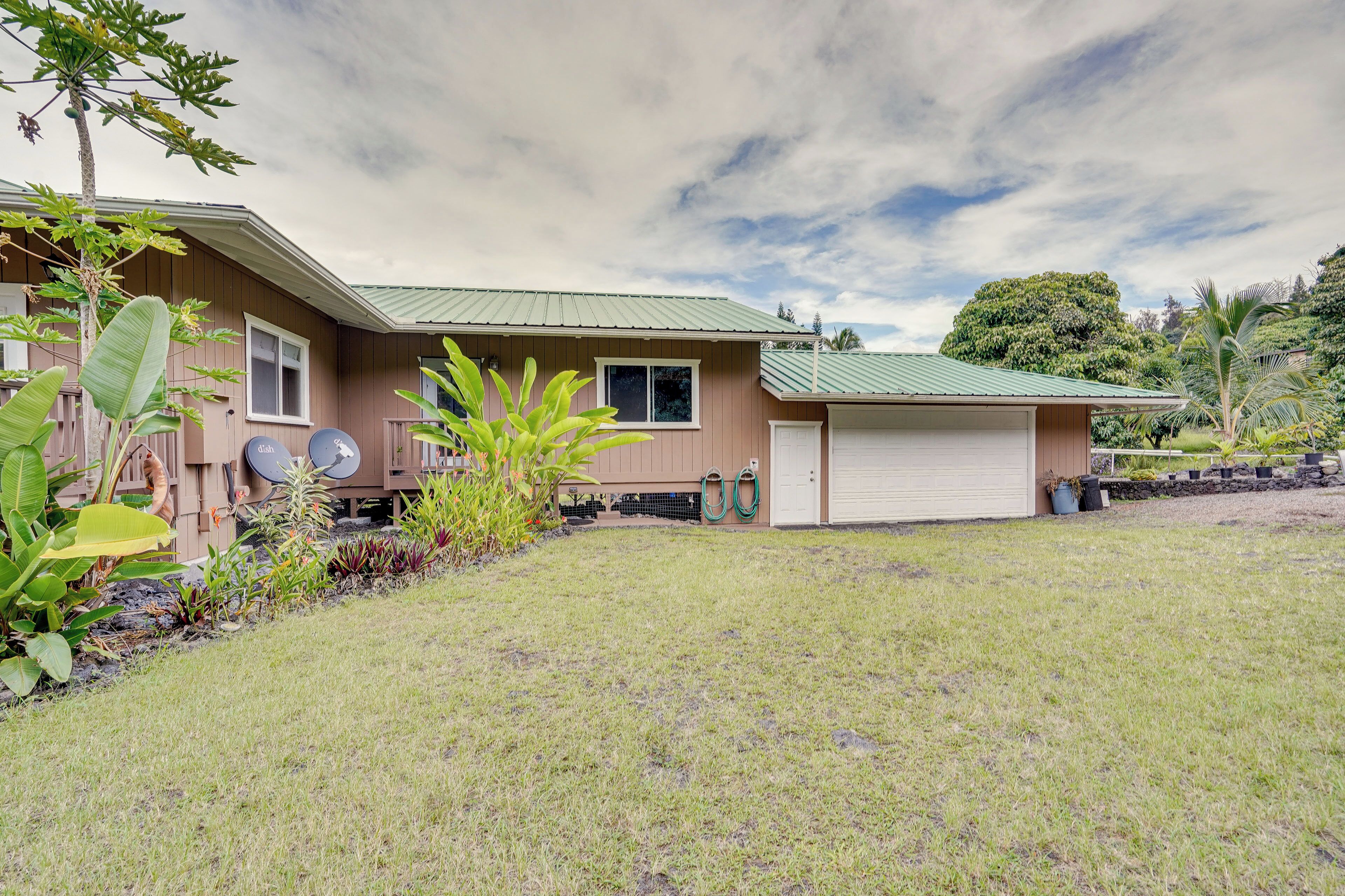 A two-story house with a garage, surrounded by a well-maintained lawn and tropical plants.
