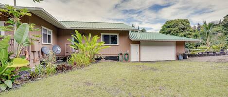 A two-story house with a garage, surrounded by a well-maintained lawn and tropical plants.