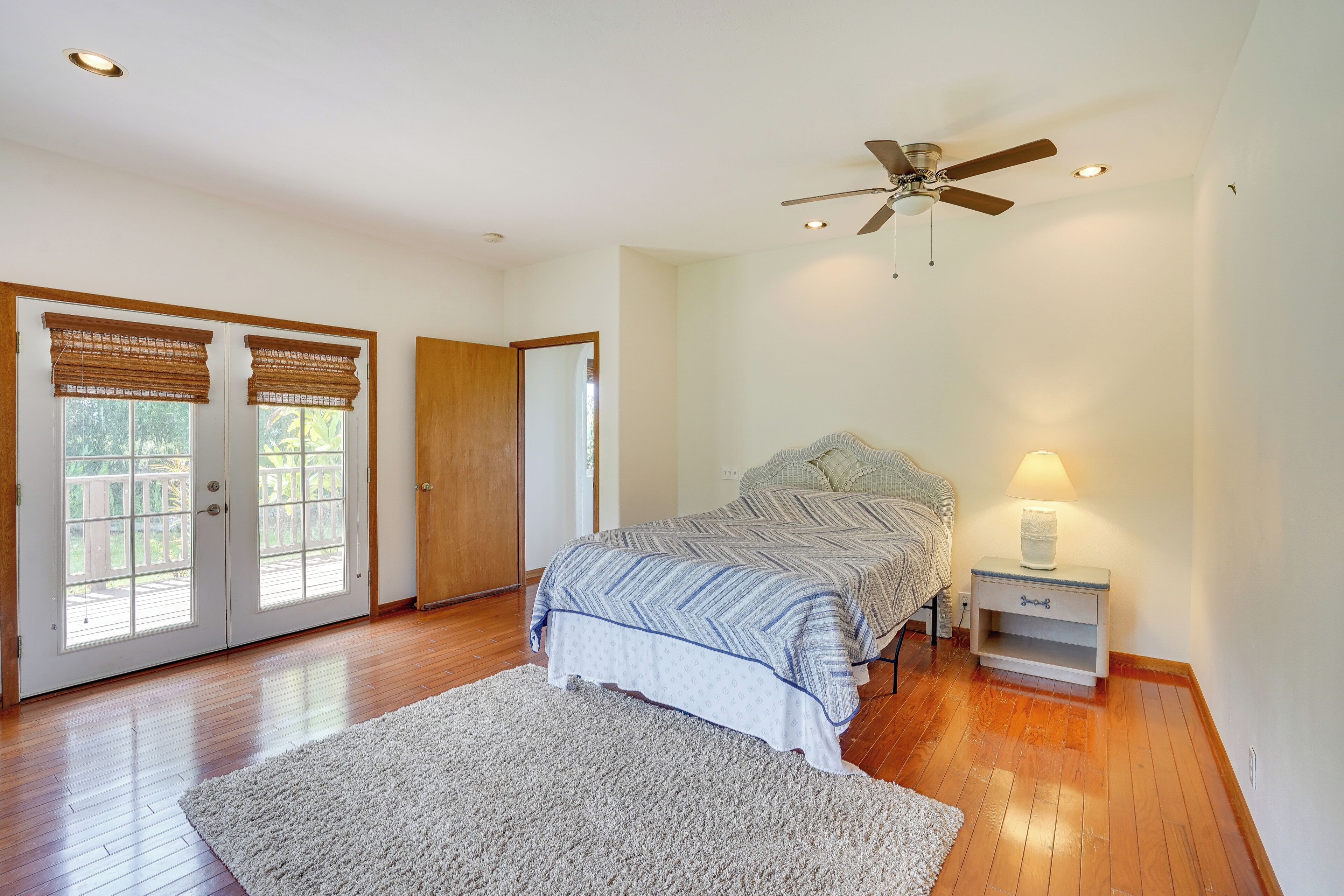 A bedroom with a bed, a nightstand, a ceiling fan, and a large window with blinds.