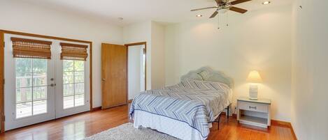 A bedroom with a bed, a nightstand, a ceiling fan, and a large window with blinds.