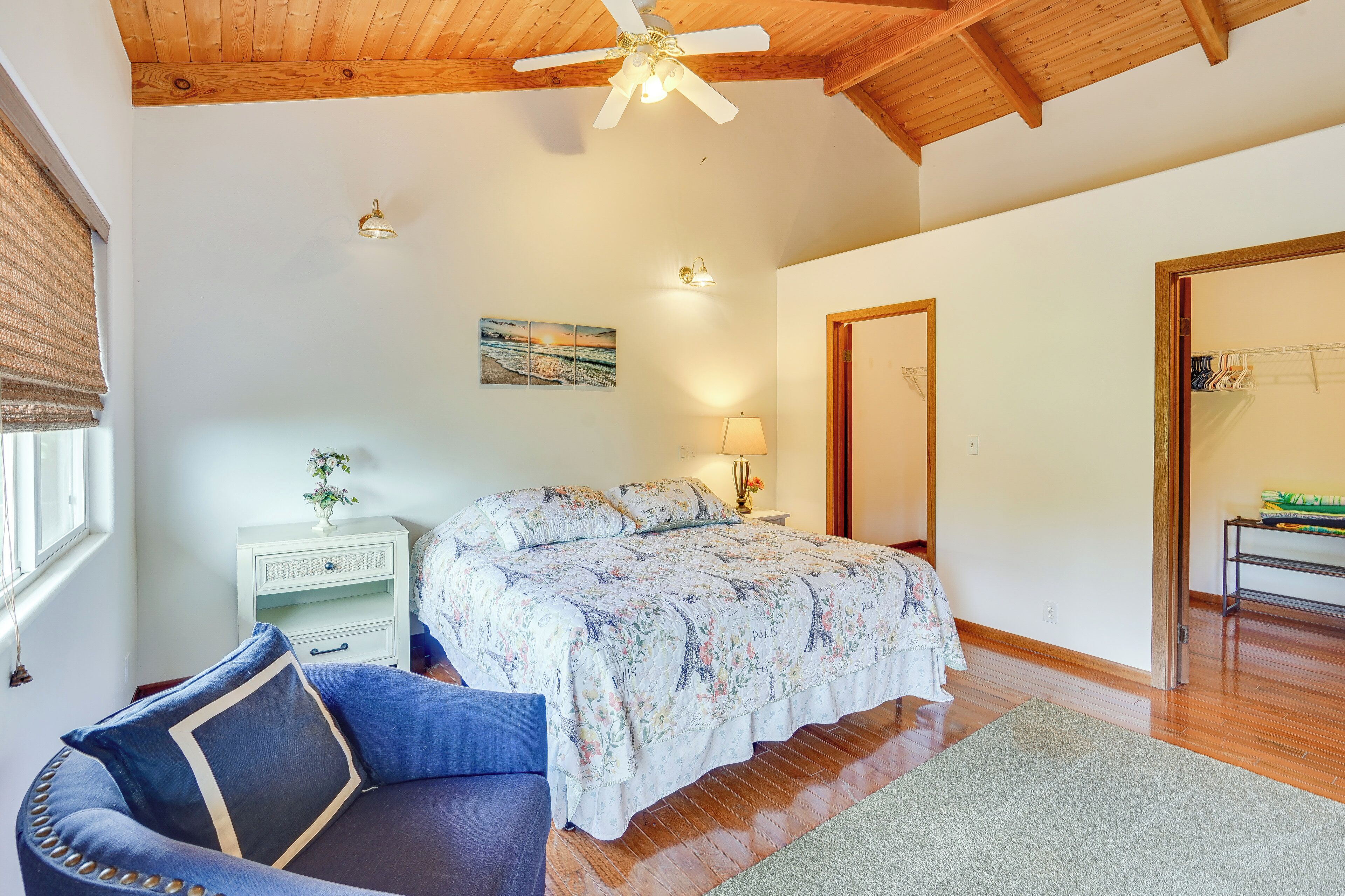 A bedroom with a bed, a nightstand, a chair, a ceiling fan, and a door leading to another room.